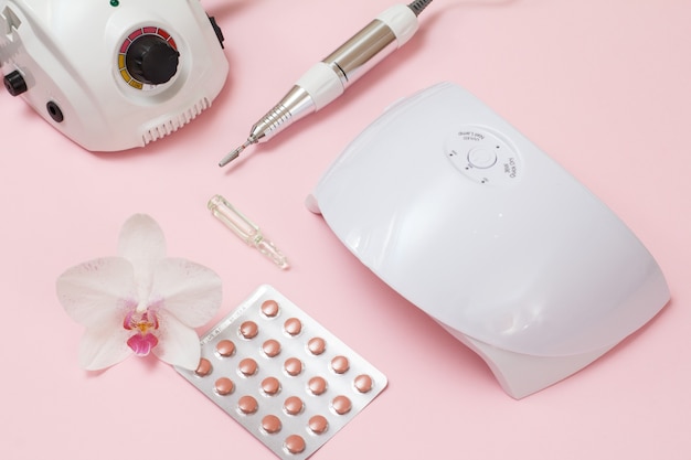 Fresa, lámpara UV led, vitaminas y flor de orquídea sobre fondo rosa. Un conjunto de herramientas cosméticas para manicura de hardware profesional. Vista superior.