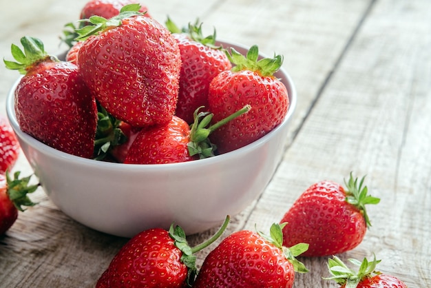 Fresa madura en un recipiente sobre la mesa de madera con espacio de copia, frutas de verano