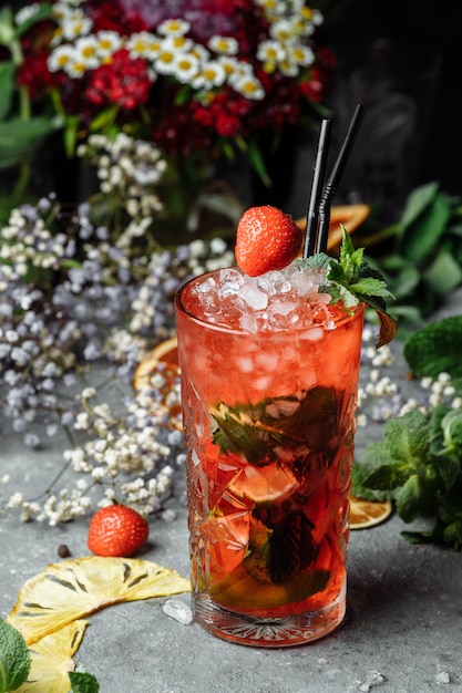 Fresa Mojito. Cóctel de mojito frío de verano con fresas, menta, limón y hielo en un vaso sobre una mesa. sobre un fondo oscuro