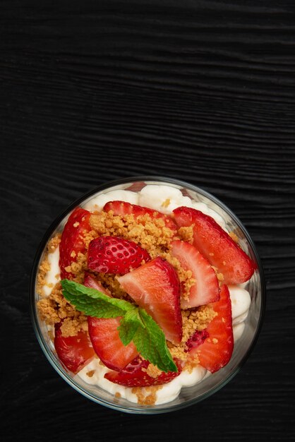 Fresa con postre de galleta y crema decorada con hoja de menta sobre fondo de madera negra con co ...