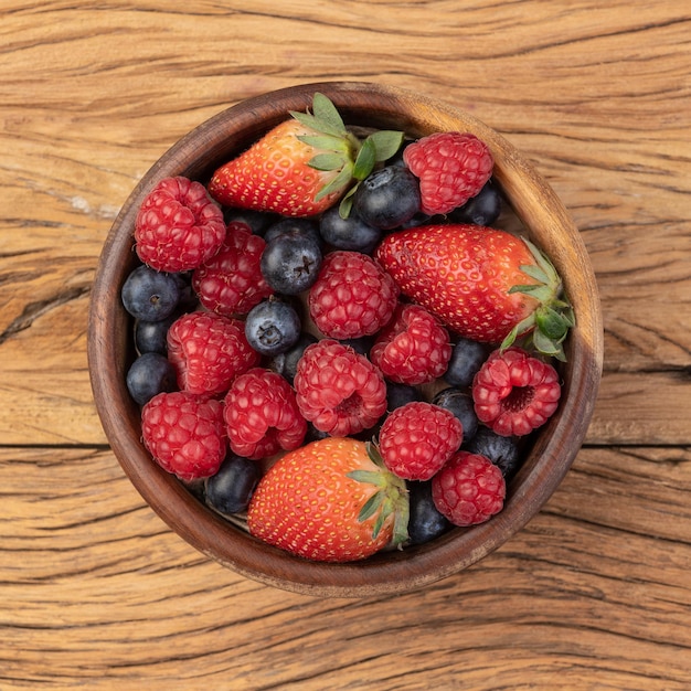 Fresas, arándanos y frambuesas en un recipiente sobre la mesa de madera.