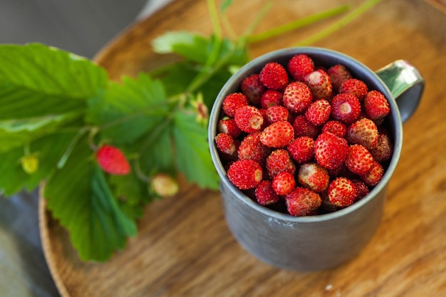 Fresas del bosque en una taza de metal en una vista superior de la bandeja de madera