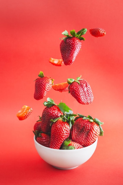 Las fresas caen en un cuenco blanco con un fondo rojo vibrante.