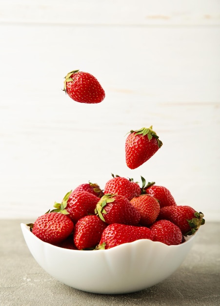 Foto las fresas caen en un tazón sobre fondo claro foto vertical