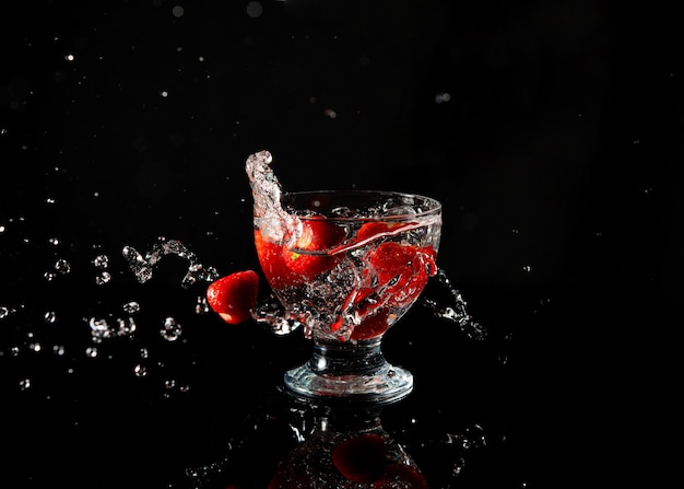 Fresas cayendo en un vaso de agua con un toque sobre un fondo negro