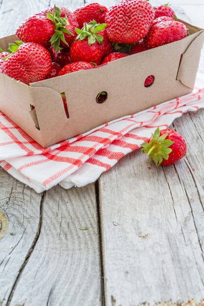 Foto fresas en cesta de cartón, fondo de madera rústica.