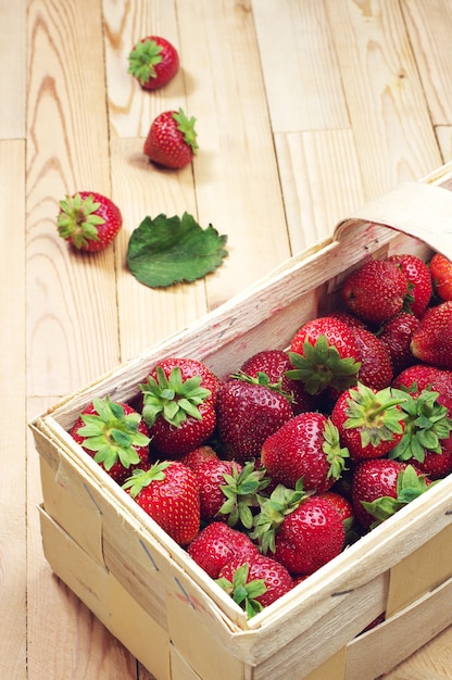 Fresas en una cesta de mimbre y cerca de una mesa de madera