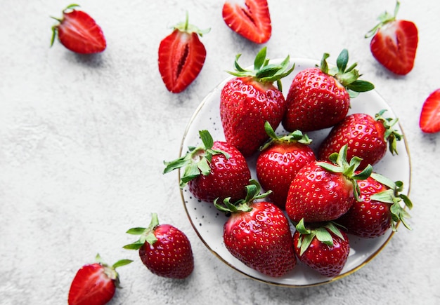 Fresas deliciosas maduras frescas en una placa blanca sobre un fondo de piedra gris