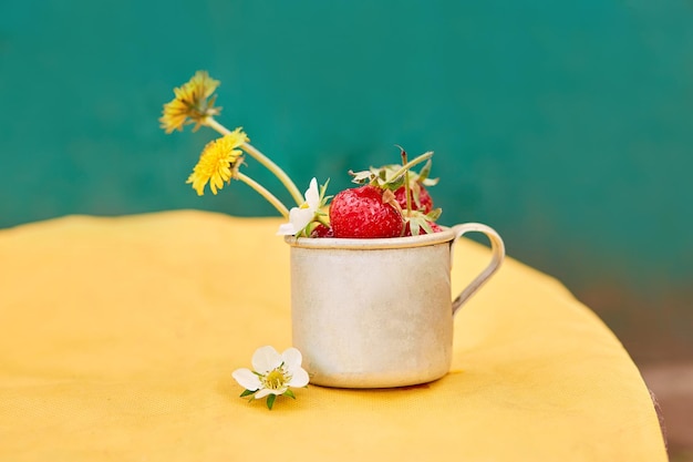 Fresas y dientes de león en una taza de viaje de aluminio metálico Fondo de primavera verde y amarillo Concepto de estética Cottagecore fondo de sombras de moda Espacio de copia Foto de alta calidad