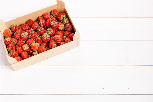 Fresas frescas en una caja de madera sobre fondo blanco.