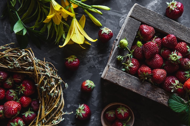 Fresas frescas en una caja vieja sobre una superficie gris con flores amarillas. Comida sana, fruta