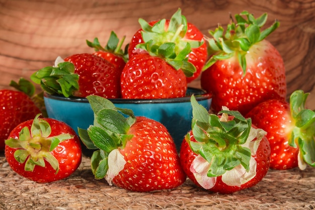 Fresas frescas con gotas de agua en un recipiente azul sobre una mesa de madera luz solar natural enfoque selectivo fresa temporada de primavera