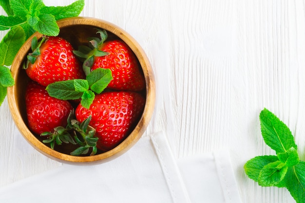 Fresas frescas en hojas de madera del cuenco y de menta en el fondo de madera blanco.