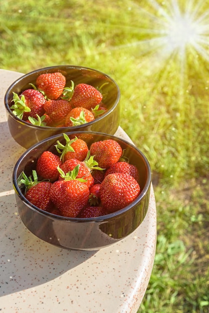 Fresas frescas, iluminadas por la luz del sol, en platos negros sobre una mesa de granito.