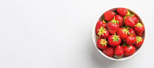 Fresas frescas y jugosas en un tazón blanco sobre un fondo gris