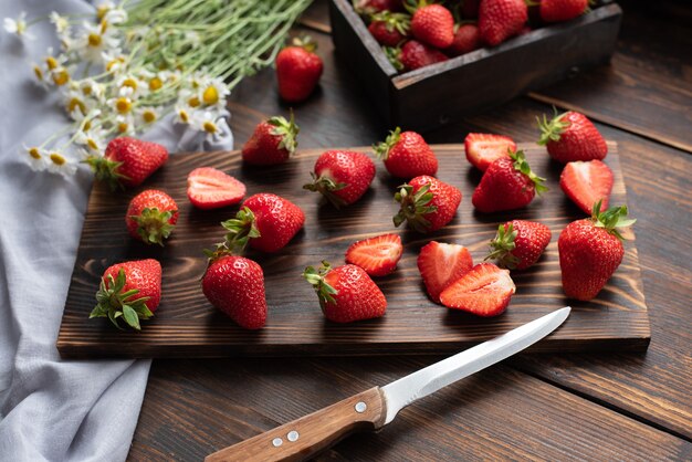 Fresas frescas en una mesa de madera en la cocina con un ramo de margaritas y textiles, concepto de verano, de cerca.