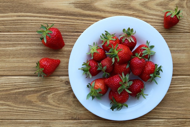 Fresas frescas en un plato sobre una mesa de madera, vista superior