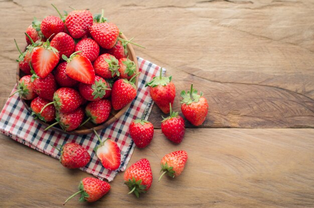 Fresas frescas en un recipiente en el fondo de madera.