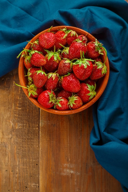 Fresas grandes frescas en una placa de arcilla sobre una mesa de madera.