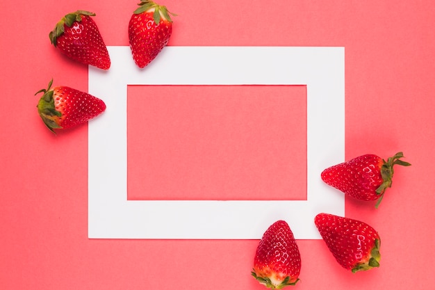 Foto fresas jugosas brillantes en el marco blanco en un fondo rosado