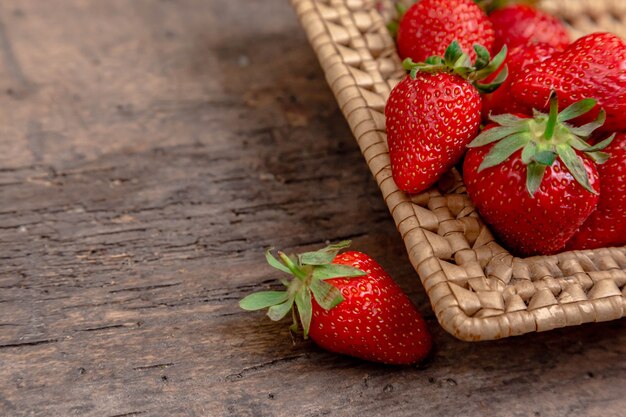 Fresas jugosas frescas en la cesta. Cesta de mimbre llena de fresas recién cosechadas sobre fondo de madera vintage