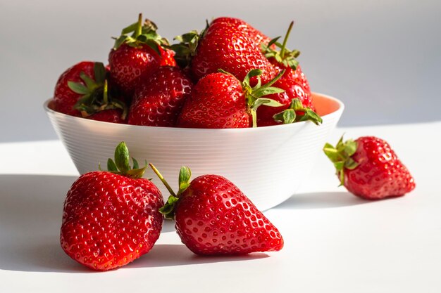 Fresas jugosas maduras en una taza blanca sobre un fondo gris claro