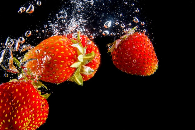 Las fresas maduras caen al agua levantando salpicaduras y burbujas de aire