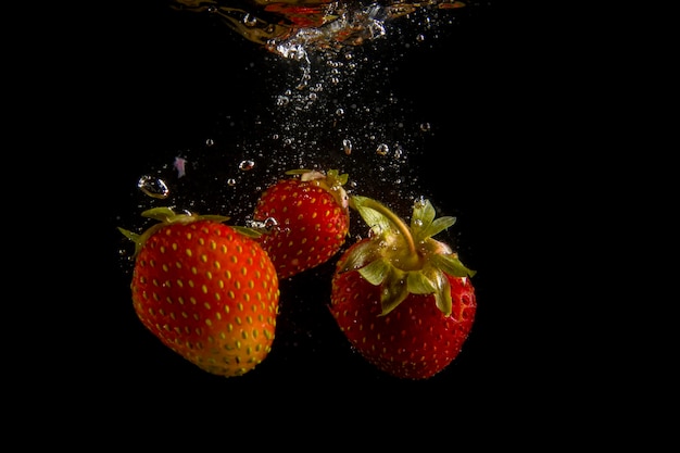 Las fresas maduras caen al agua levantando salpicaduras y burbujas de aire
