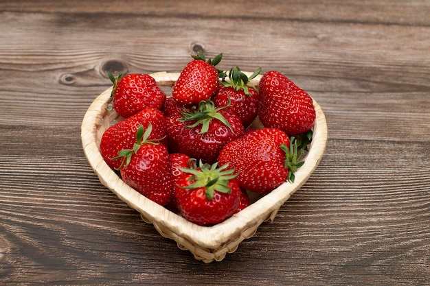 Fresas maduras en una canasta en forma de corazón sobre una mesa de madera