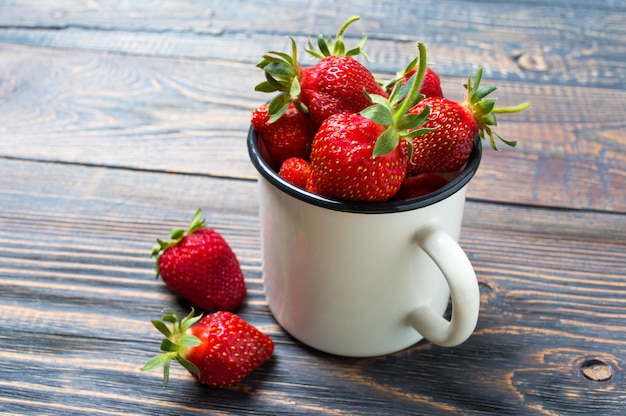 Fresas maduras frescas en una taza rústica en una mesa de madera. Cultivo recién cosechado.