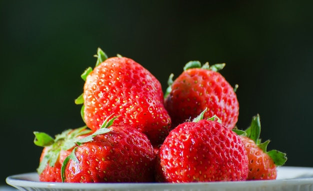 Fresas maduras con hojas en cesta de mimbre en la mesa de madera sobre fondo borroso