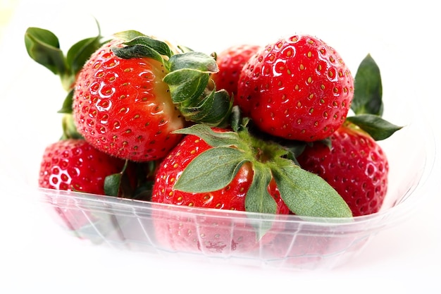 Fresas maduras en un paquete de plástico sobre un fondo blanco Deliciosas bayas frescas en un recipiente para la venta a los clientes Mantener los alimentos frescos Alimentos saludables vitaminas y microelementos