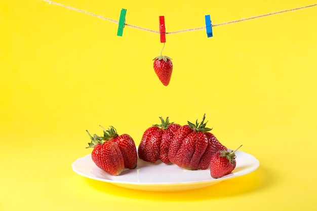 Fresas maduras en plato blanco y pinzas para la ropa