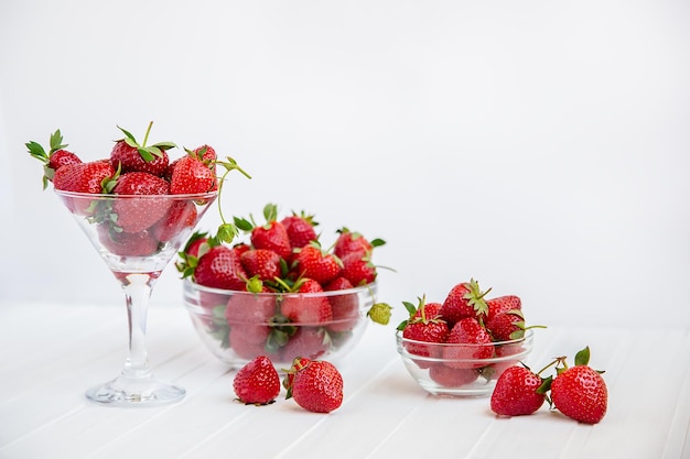 Fresas maduras rojas en un recipiente de vidrio sobre una mesa de madera blanca Cosecha de tu jardín