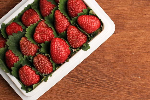 Fresas orgánicas agrupadas recién cosechadas con hojas verdes en una caja blanca del supermercado. Fondos y papel tapiz de alimentos saludables, espacio para copiar texto