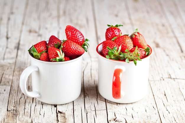 Fresas orgánicas rojas en dos tazas de cerámica blanca.