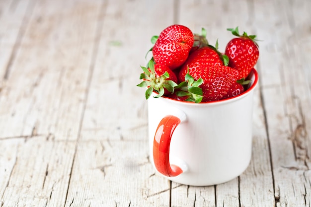 Fresas orgánicas rojas en taza de cerámica blanca.
