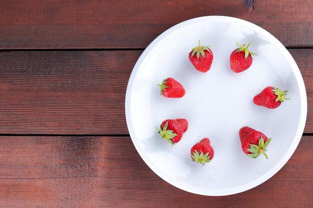 Fresas en plato blanco Fresas rojas sobre fondo de madera Espacio de copia