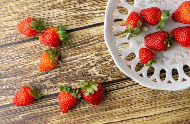 Fresas en un plato decorado y sobre una mesa de madera