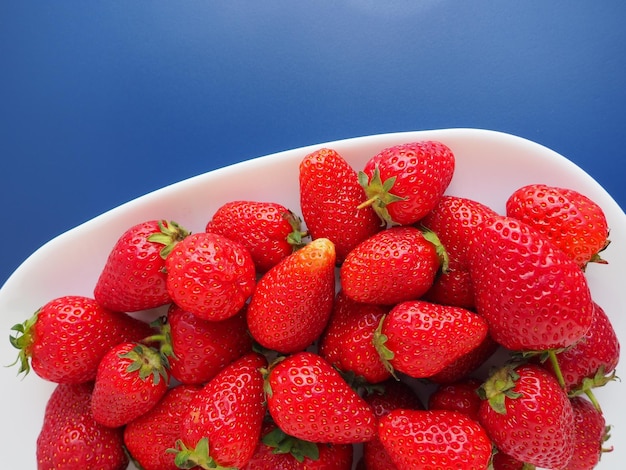 Fresas en un plato de fondo azul, platos blancos y un gran jardín rojo delicioso maduro