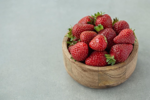 Fresas en un plato de madera sobre un fondo gris