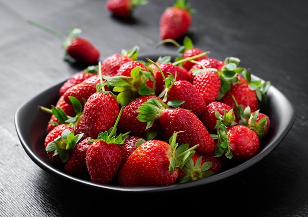 Fresas en un plato negro sobre fondo oscuro