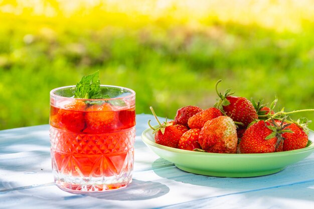 Fresas en plato sobre mesa y bebida fresca con menta