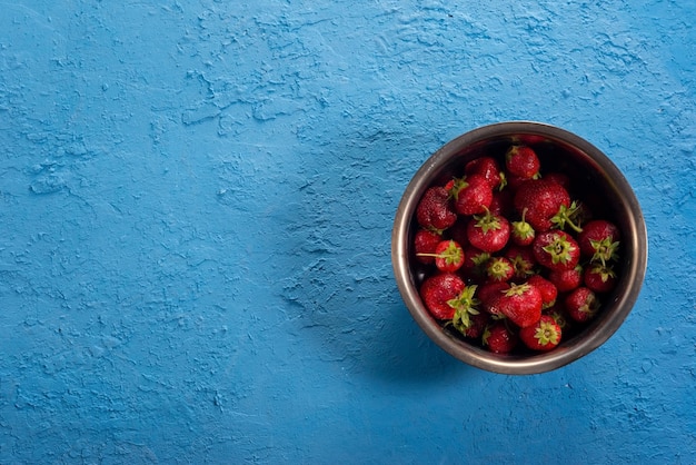 Fresas en un recipiente de metal sobre un fondo azul Vista desde arriba