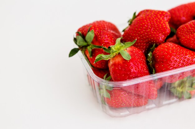 Fresas en un recipiente de plástico sobre un fondo claro, fruta fea