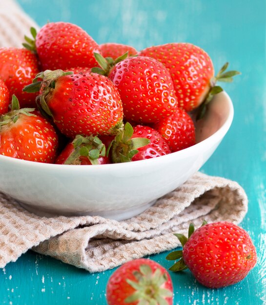 Fresas en un recipiente sobre la mesa de madera turquesa de cerca