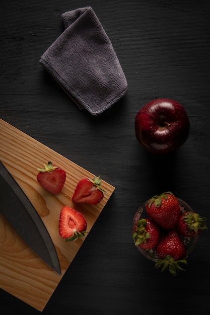 Fresas en un recipiente sobre una mesa con una tabla de cortar y un cuchillo al lado