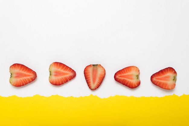 Fresas en rodajas sobre fondo amarillo con borde de papel blanco rasgado Fondo de verano