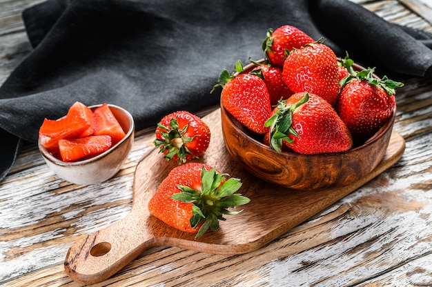 Fresas rojas en un cuenco de madera sobre una tabla de cortar. Fondo blanco. Vista superior.