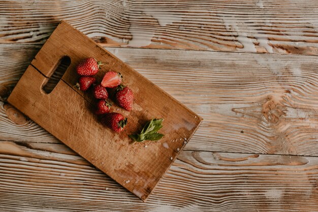 Fresas rojas frescas jugosas esparcidas sobre la mesa con tablón vintage. hoja de menta. gotas y salpicaduras de leche derramada.